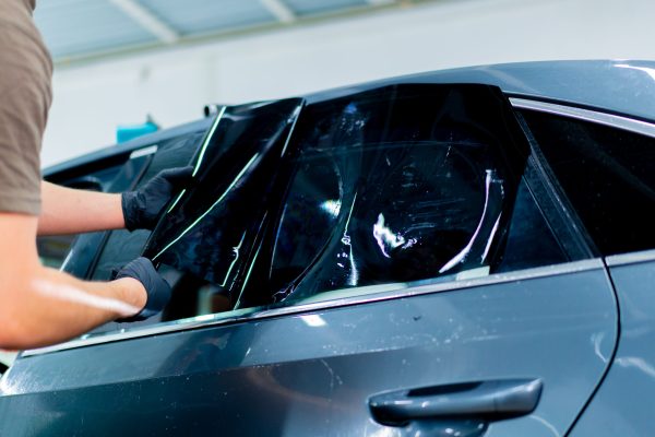 a car mechanic carefully sticks a protective tinted film on a car glass at detailing station