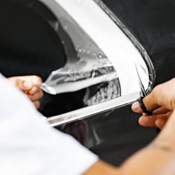 Car wrapping specialist wraps a car with adhesive film in car detailing service, close up