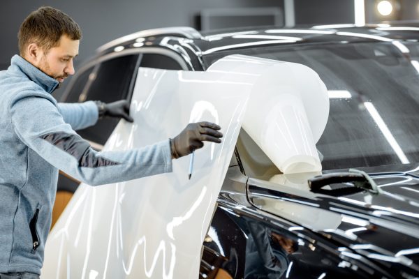 Man preparing protective film for sticking on a car body, taking it from the roll at the vehicle service station. Concept of car body protection with special films