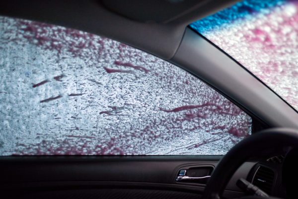 Man washing his car, using pink active foam on self service washing, contactless high pressure water jet.